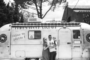 A couple and their young child posing in front of a Fripes Truck Vintage trailer in Montpellier.